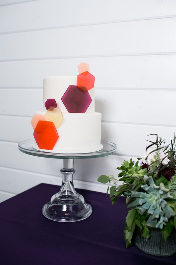 a white round wedding cake with colorful semi sheer hexagons that give a fresh and bold modern feel to it