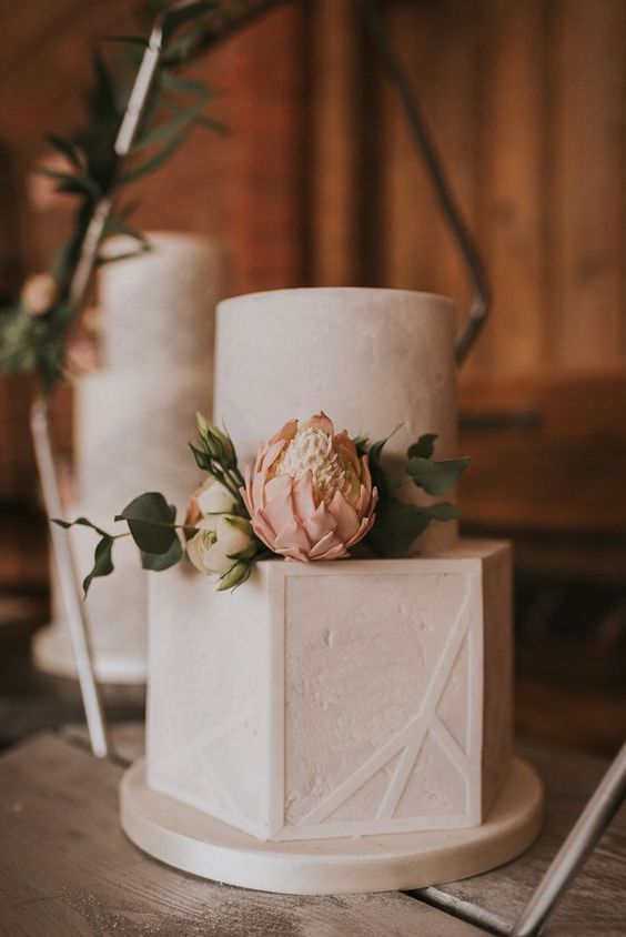 a white textural buttercream wedding cake with white and blush blooms and greenery and with geometric patterns is a lovely idea