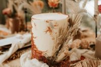 a white wedding cake with rust sugar decorating and dried grasses and fronds is a lovely idea for a boho wedding
