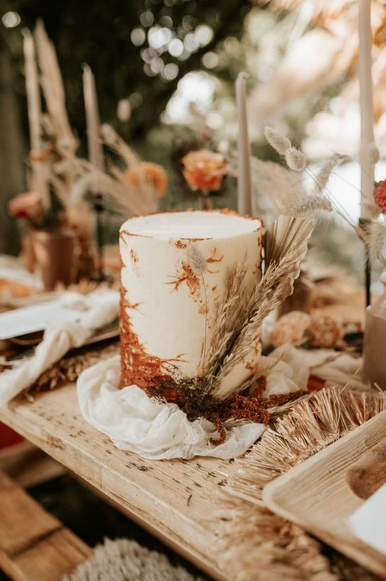 a white wedding cake with rust sugar decorating and dried grasses and fronds is a lovely idea for a boho wedding
