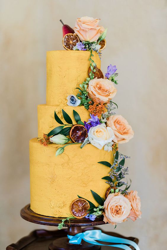 a yellow textural wedding cake with pastel and bold blooms, greenery and dried citrus slices is super cool
