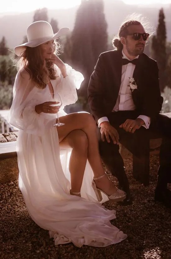 an elegant and whimsy bridal look with a flowy and semi sheer wedding dress, silver heels and a white hat is amazing