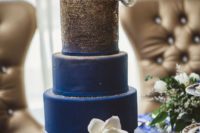 an elegant ombre wedding cake from gold glitter to navy decorated with a single white sugar bloom