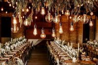 Edison bulbs hanging down from greenery chandeliers are amazing to light up any rustic or boho wedding venue, not only a barn