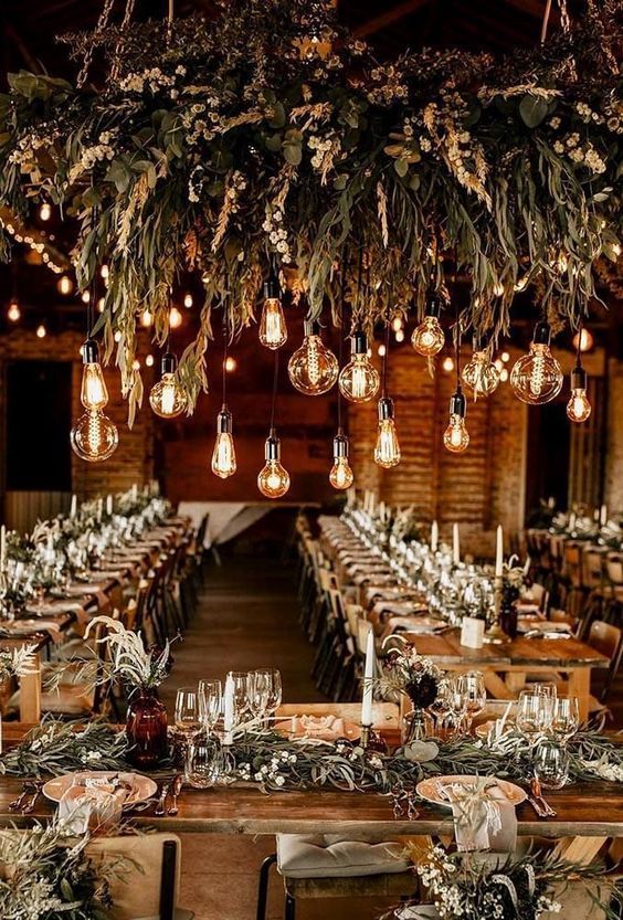 Edison bulbs hanging down from greenery chandeliers are amazing to light up any rustic or boho wedding venue, not only a barn