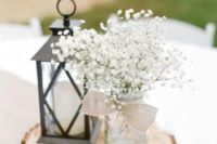 a barn wedding centerpiece of a wood slice, a candle lantern, a jar with a burlap bow and baby’s breath