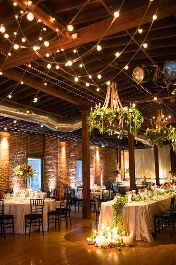 a barn wedding venue lit up with string lights and refined greenery chandeliers and candles on the floor is a spectacular idea