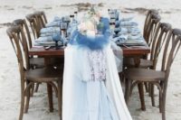 a beach bridal shower table with a driftwood, bloom and candle unstallation, blue glasses and linens and pink blooms