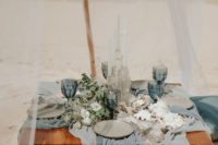a beach wedding picnic with a low table, airy blue and grey runners, blue glasses, greenery, shells and corals