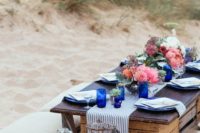 a beach wedding picnic with a low table, pillows, candles, bright blooms, blue vases and striped linens