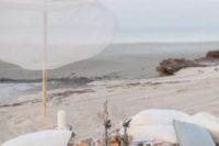 a beach wedding picnic with a pallet table, white and blue pillows, pillar candles, neutral blooms and candles