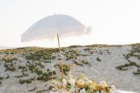 a beach wedding picnic with white and blue pillows, an airy runner, neutral blooms and greenery, an umbrella