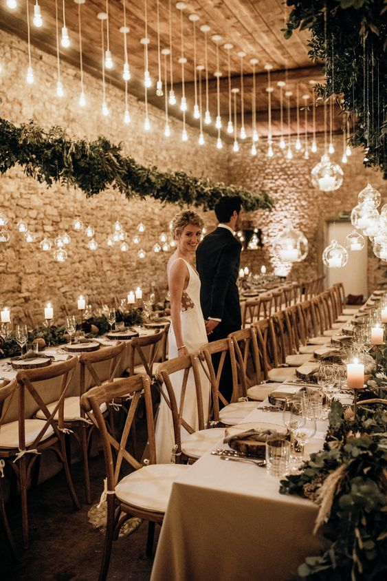 a beautiful barn wedding venue with Edison bulbs hanging down, bubble candleholders and pillar candles on the table