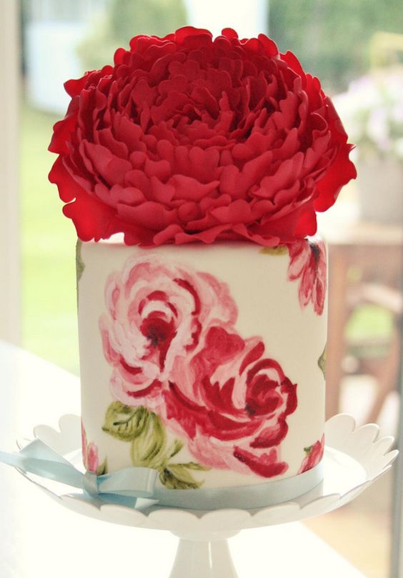 a beautiful wedding cake with painted pink and red blooms and an oversized flower on top is amazing for a flower filled wedding