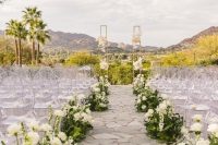 a beautiful wedding ceremony space with a wedding altar decorated with blooms, greenery and white flower arrangements lining up the aisle