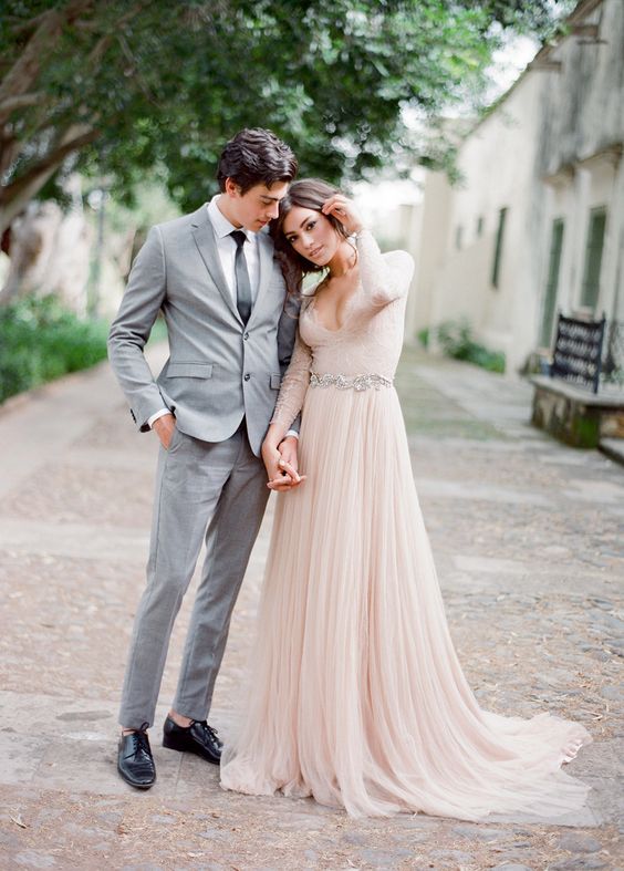 a blush A line wedding dress with a lace bodice, a plunging neckline, long sleeves and a layered skirt plus a train