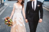 a blush wedding dress with an illusion neckline, sleeves and white floral appliques all over the dress that make it edgy