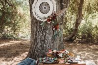 a boho woodland wedding picnic with a dream catcher, bright blooms and pampas grass, a low table, pastel pillows and colored glasses