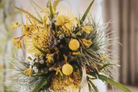 a bold textural wedding bouquet of greenery, pincushion proteas, billy balls and other yellow blooms for a spring or summer bride