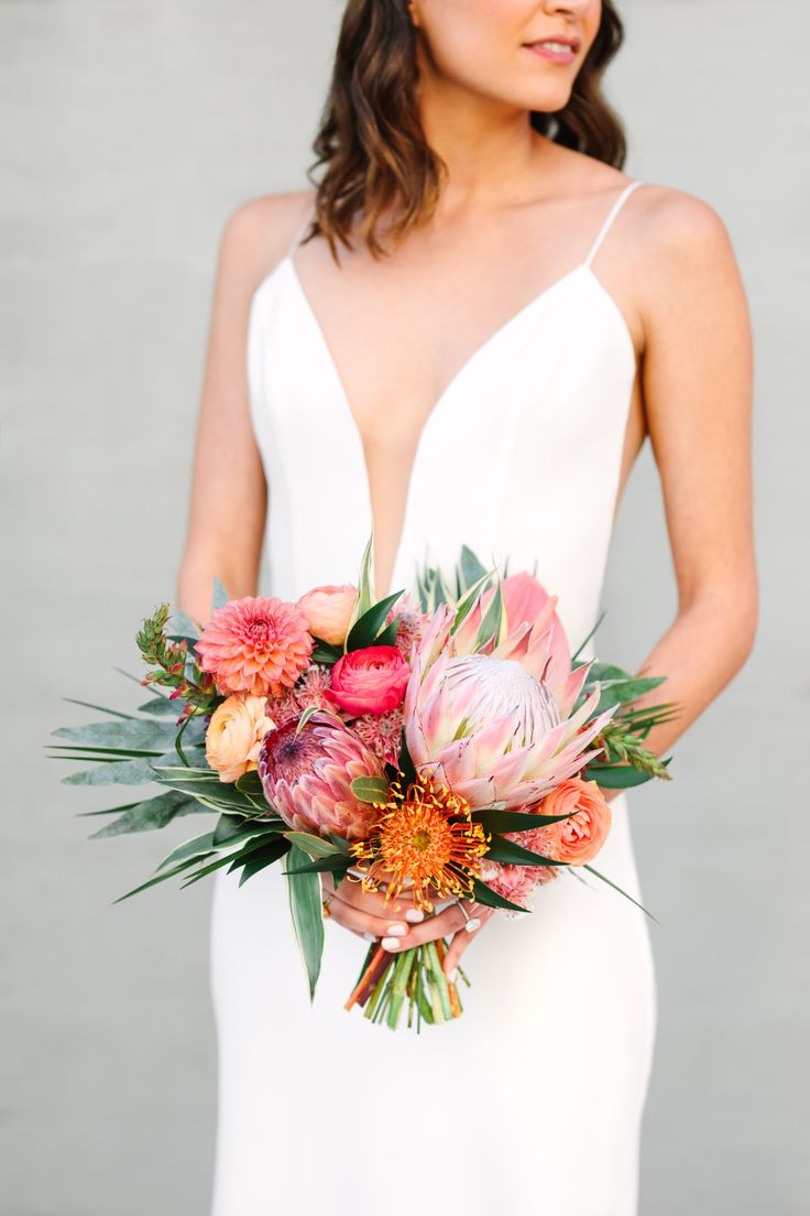 a bold tropical wedding bouquet of a pincushion and king protea, greenery, ranunculus and leaves is a stylish idea