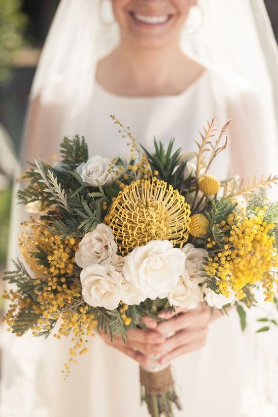 a bold wedding bouquet of white roses, pincushion proteas, billy balls and mimosas, greenery is a cool idea for spring or summer