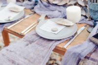 a bright beach bridal shower table with lavender linens, blue glasses, candles and seashells looks unusual