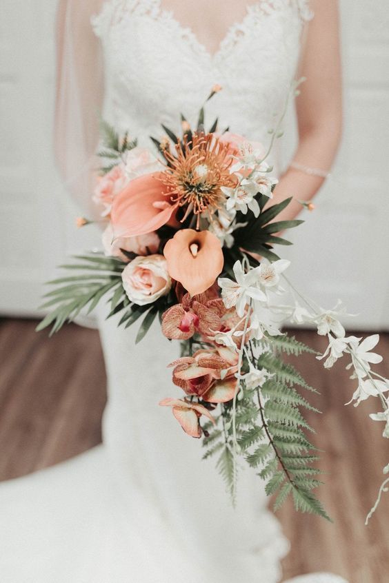 a cascading tropical wedding bouquet of pink callas and roses, pincushion proteas, orchids, greenery and white blooms
