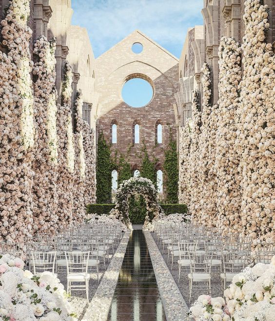 a castle courtyard with pillars fully covered with blush and neutral blooms, with a lush floral wedding arch