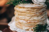 a chic and simple crepe wedding cake with sugar powder, greenery and white blooms on top is a great idea for a woodland wedding