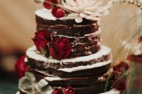 a chocolate naked wedding cake topped with red roses, greenery and succulents is a lovely rustic wedding idea