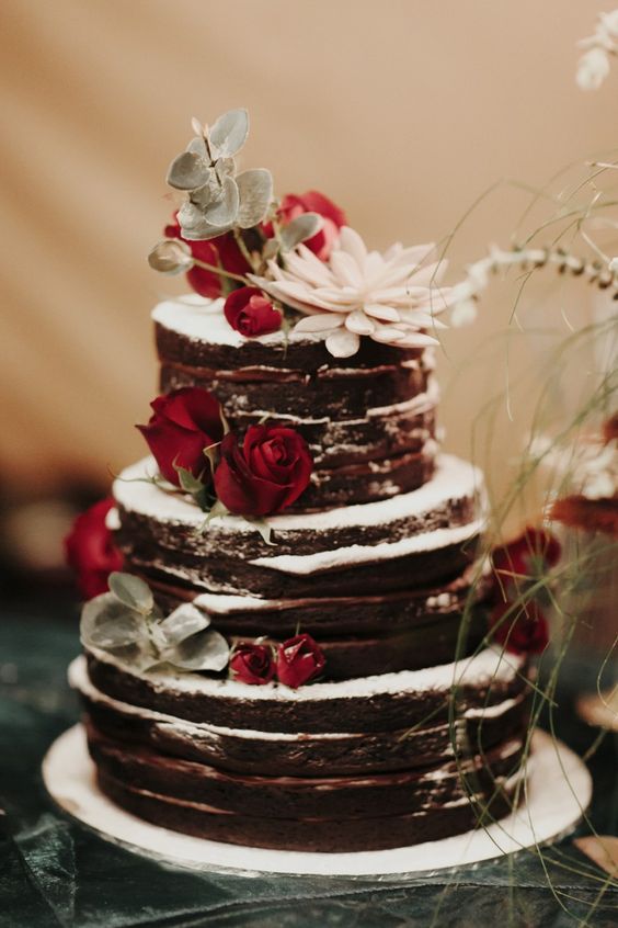 a chocolate naked wedding cake topped with red roses, greenery and succulents is a lovely rustic wedding idea