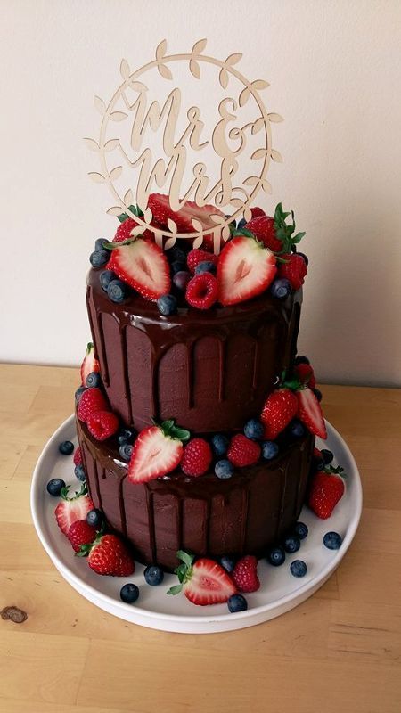a chocolate wedding cake with chocolate drip, fresh berries and a calligraphy cake topper is a fantastic and delicious-looking idea for a wedding