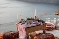 a coastal wedding picnic with a biew, leather ottomans, bright pillows, pink candles and napkins plus greenery