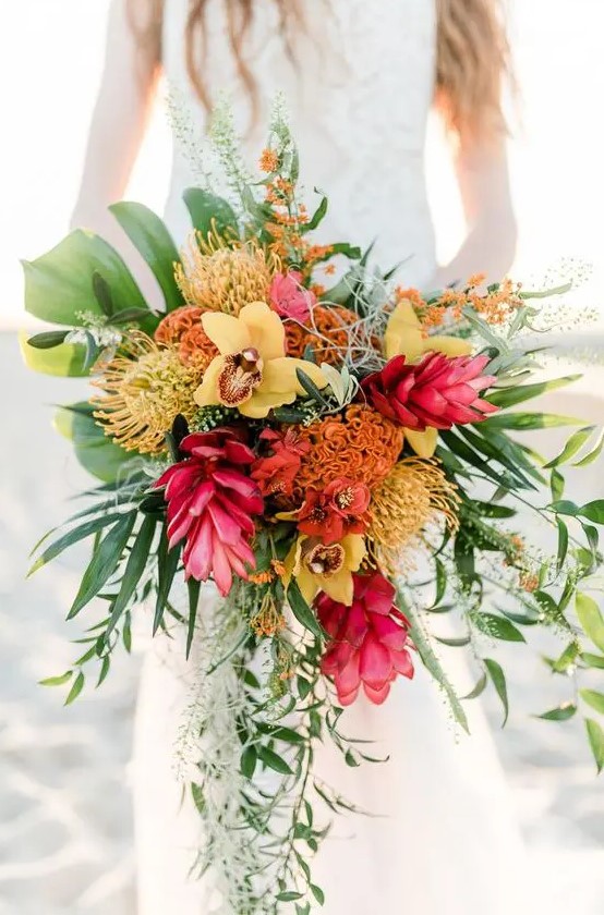 a colorful tropical wedding bouquet of yellow orchids, pink and orange blooms, pincushion proteas, greenery and blooming branches