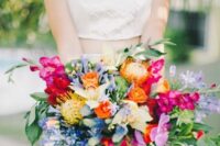 a colorful wedding bouquet of hot pink orchids, fuchsia, orange, blue and yellow blooms, pincushion proteas, greenery and ribbons