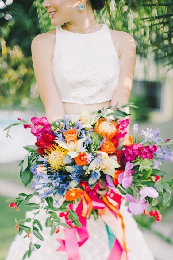a colorful wedding bouquet of hot pink orchids, fuchsia, orange, blue and yellow blooms, pincushion proteas, greenery and ribbons