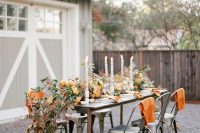 a cool fall outdoor barn wedding reception with a lush table runner of dried foliage and blooms and fruit, elegant candles and orange blankets