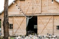 a cool outdoor barn wedding reception space with long tables and benches, with string lights over the space and white linens is welcoming