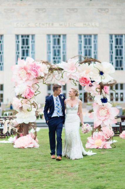 a creative wedding arch decorated with pink and white oversized blooms and twigs is a cool and chic idea for a wedding