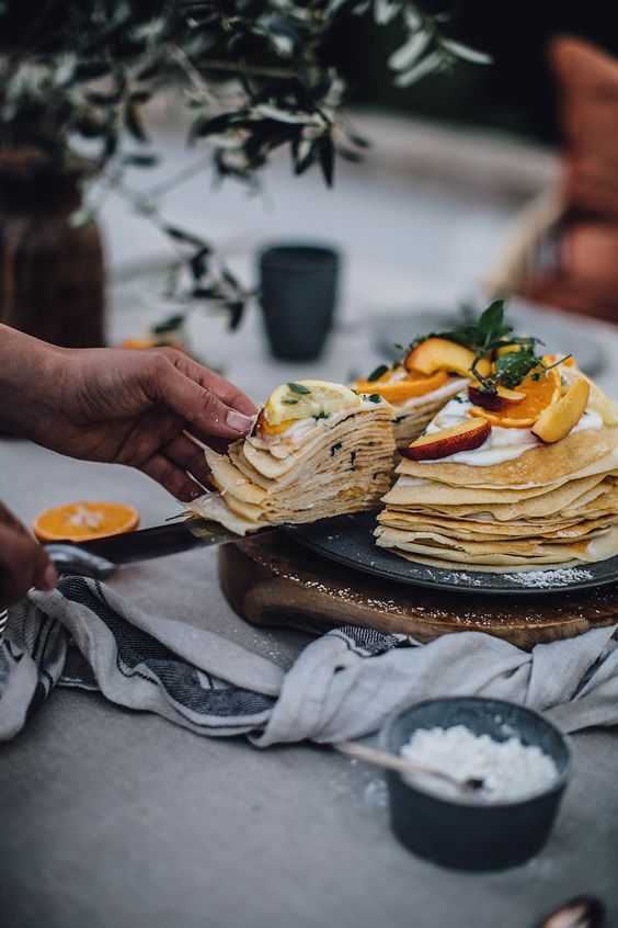 a crepe wedding cake with cream and fresh fruit slices and greenery on top is a gorgeous idea for a relaxed summer wedding