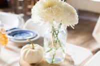 a cute barn wedding centerpiece of a wood slice, a white pumpkin and some white blooms in a jar