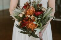 a dramatic wedding bouquet of burgundy peonies, some neutral roses, pincushion proteas, greenery and ribbons
