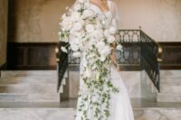 a fantastic all-white cascading wedding bouquet of peonies and ranunculus plus long greenery going down make a statement