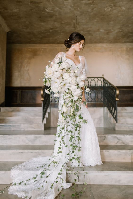A fantastic all white cascading wedding bouquet of peonies and ranunculus plus long greenery going down make a statement