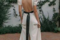 a fantastic white wedding dress with a square cutout back, puff sleeves, a slit on the back with buttons, a black sash, black flower earrings and a black bow accenting the hairstyle