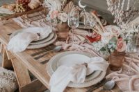 a gorgeous boho beach bridal shower table with pastel blooms, a pink table runner, woven placemats and seashell pendants over the table