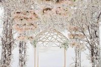 a gorgeous wedding ceremony space with lush florals forming the roof and floral chandeliers plus an arbor with curtains