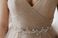 a greige shining A-line wedding dress with a draped bodice, a tulle skirt and a delicate embellished sash are a lovely and subtle combo for a bride