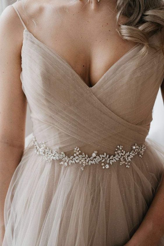 a greige shining A line wedding dress with a draped bodice, a tulle skirt and a delicate embellished sash are a lovely and subtle combo for a bride