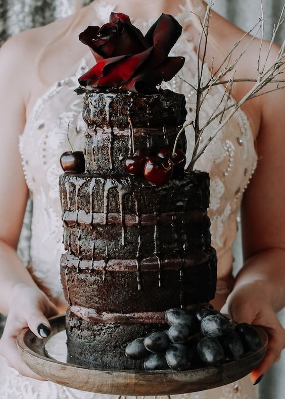 a jaw-dropping and mouth-watering dark chocolate naked wedding cake with chocolate drip, an oversized rose, branches and cherries for a Halloween wedding